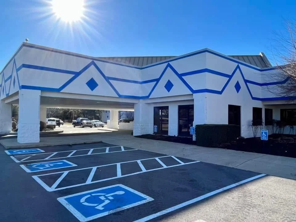 White commercial building with blue geometric roof trim, painted columns, and blue parking lot striping